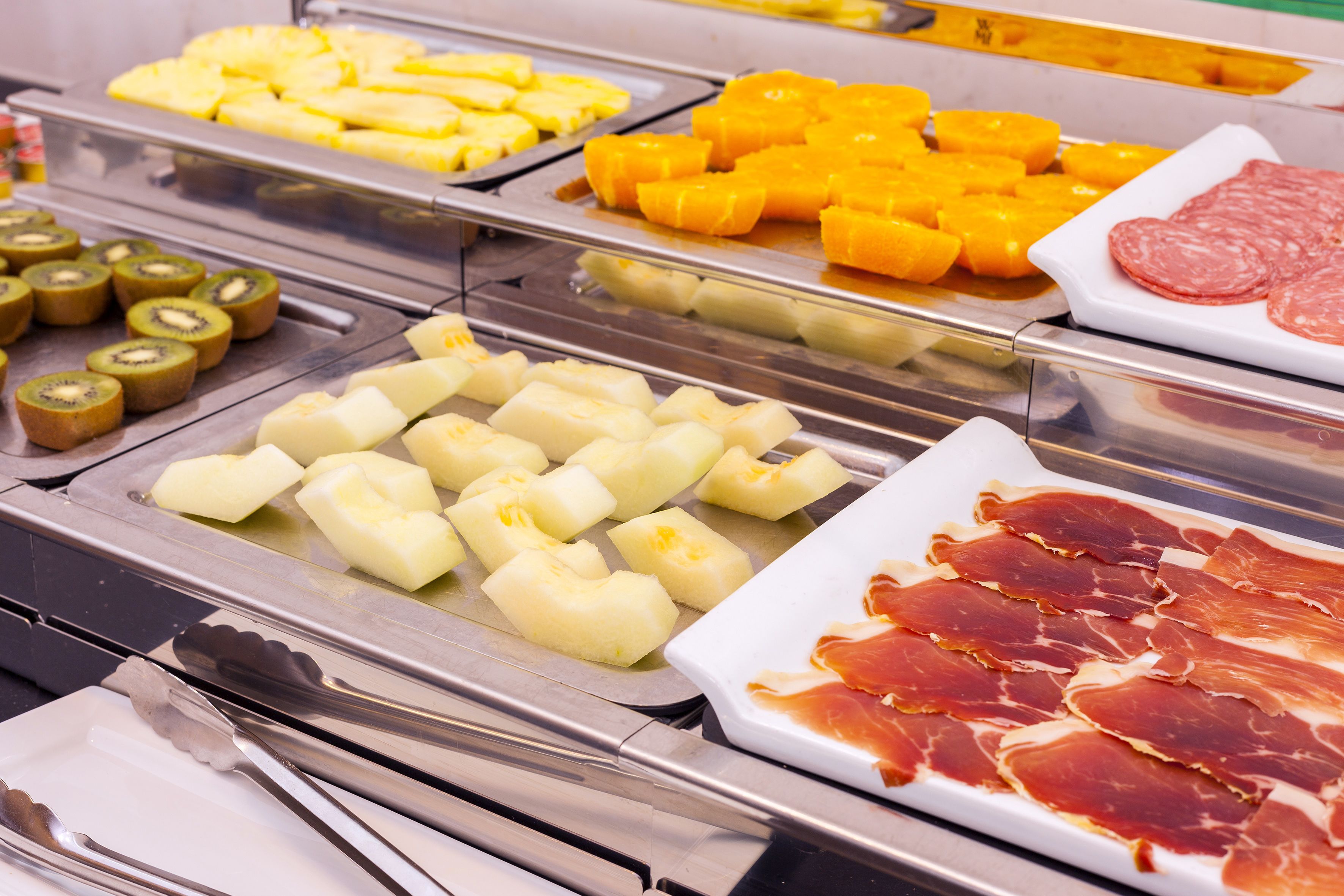 Ein Buffet mit verschiedenen Speisen, darunter Ananas, Mango, Kiwi, Käse und Wurstwaren.