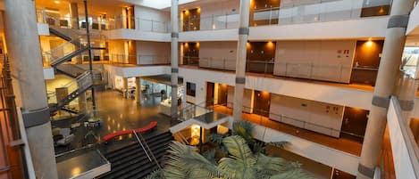 Un atrium à plusieurs niveaux, doté d’un escalier central, de nombreux balcons et de plantes d’intérieur.