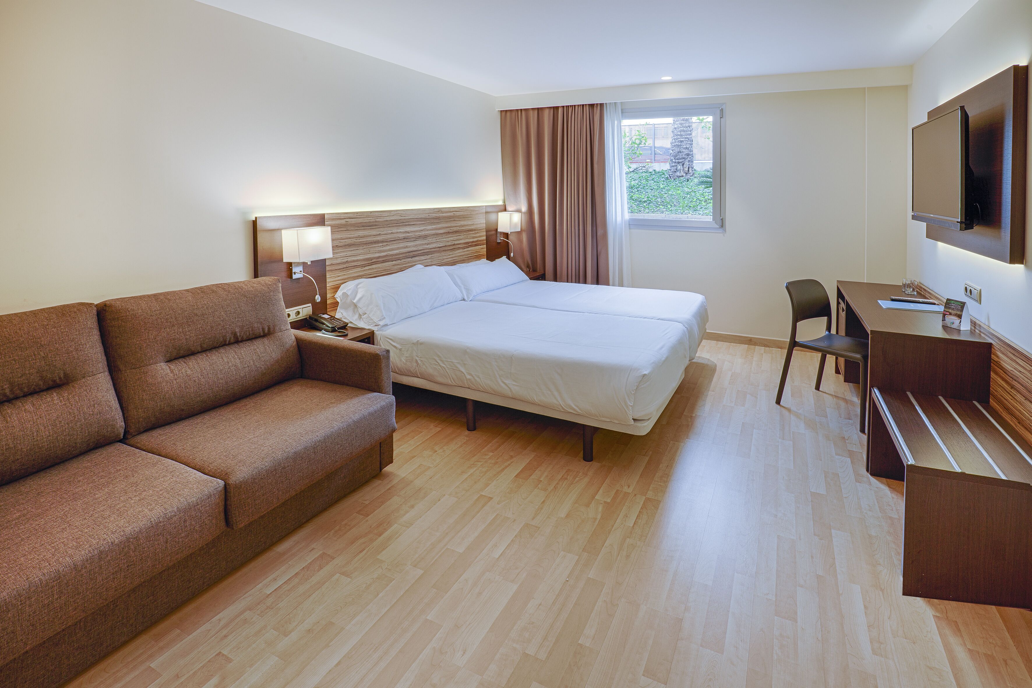 A hotel room with a bed, a sofa, a desk, and a TV.