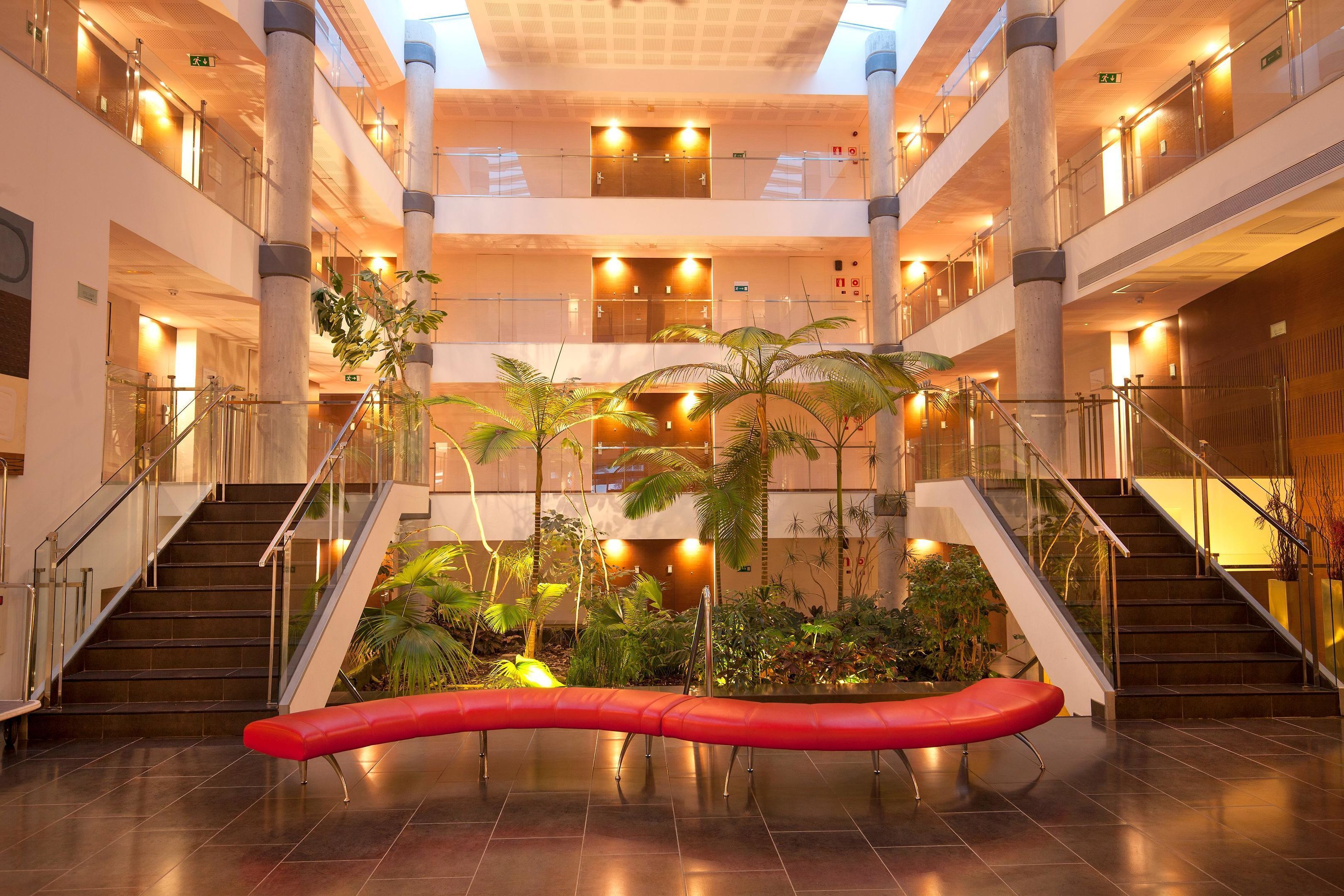 Un atrio de varios niveles con una escalera central, barandillas de vidrio y plantas de interior.