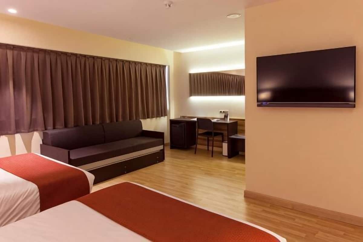 A hotel room with two beds, a sofa, a desk, a chair, a TV, and a flat-screen TV mounted on the wall.