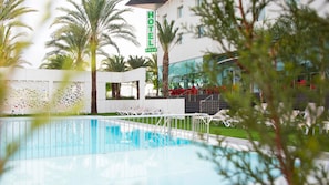 A hotel pool area with lounge chairs, palm trees, and a sign indicating the hotel name. - Hotel Port Elche (Elche)