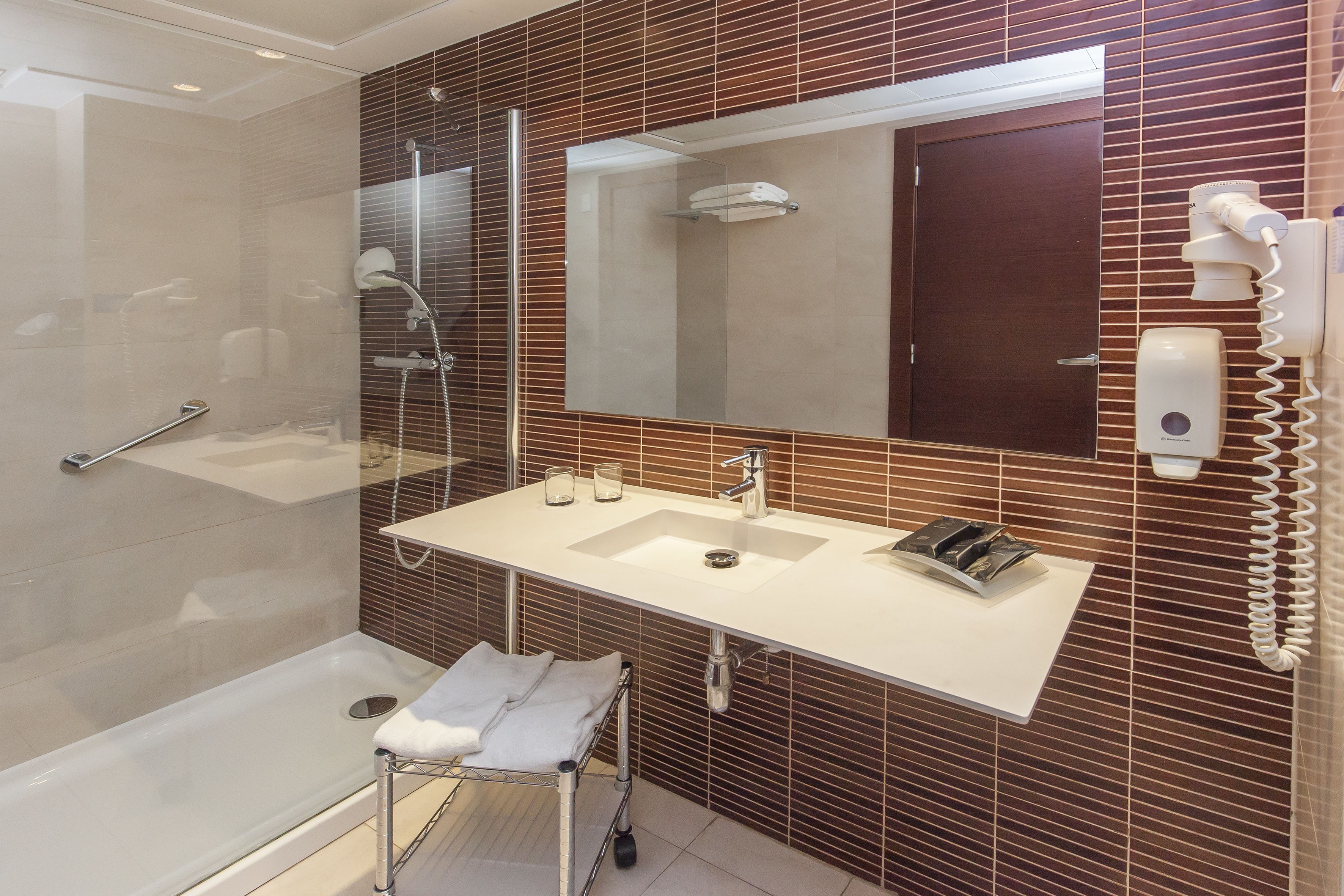 A modern bathroom with a glass-enclosed shower, a white sink with a mirror above it, and a towel rack.