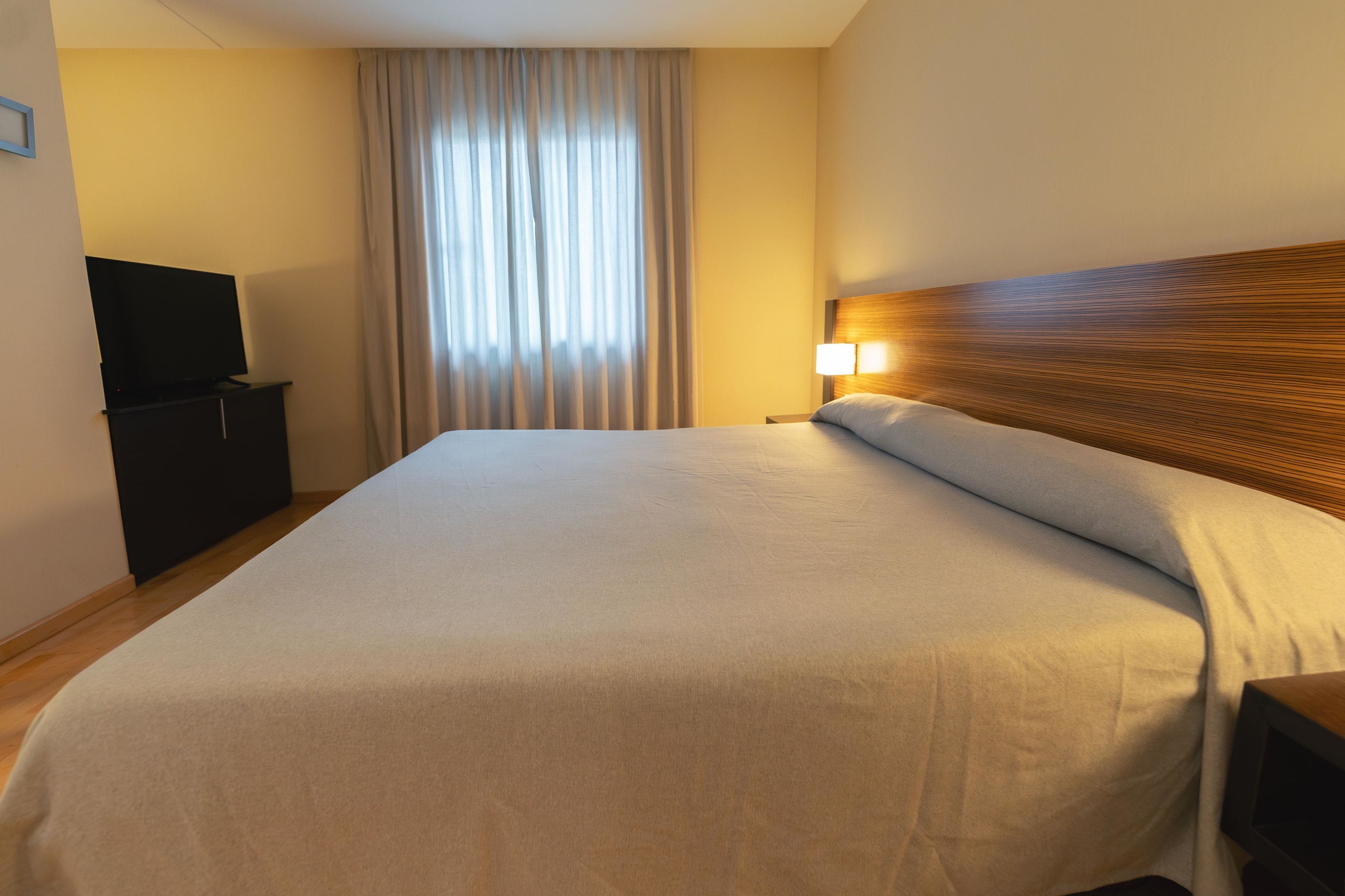 Ein Hotelzimmer mit einem großen Bett, einem Fernseher auf einem Schrank und einem Fenster mit Vorhängen.