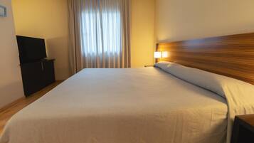 A hotel room with a large bed, a television on a cabinet, and a window with curtains.