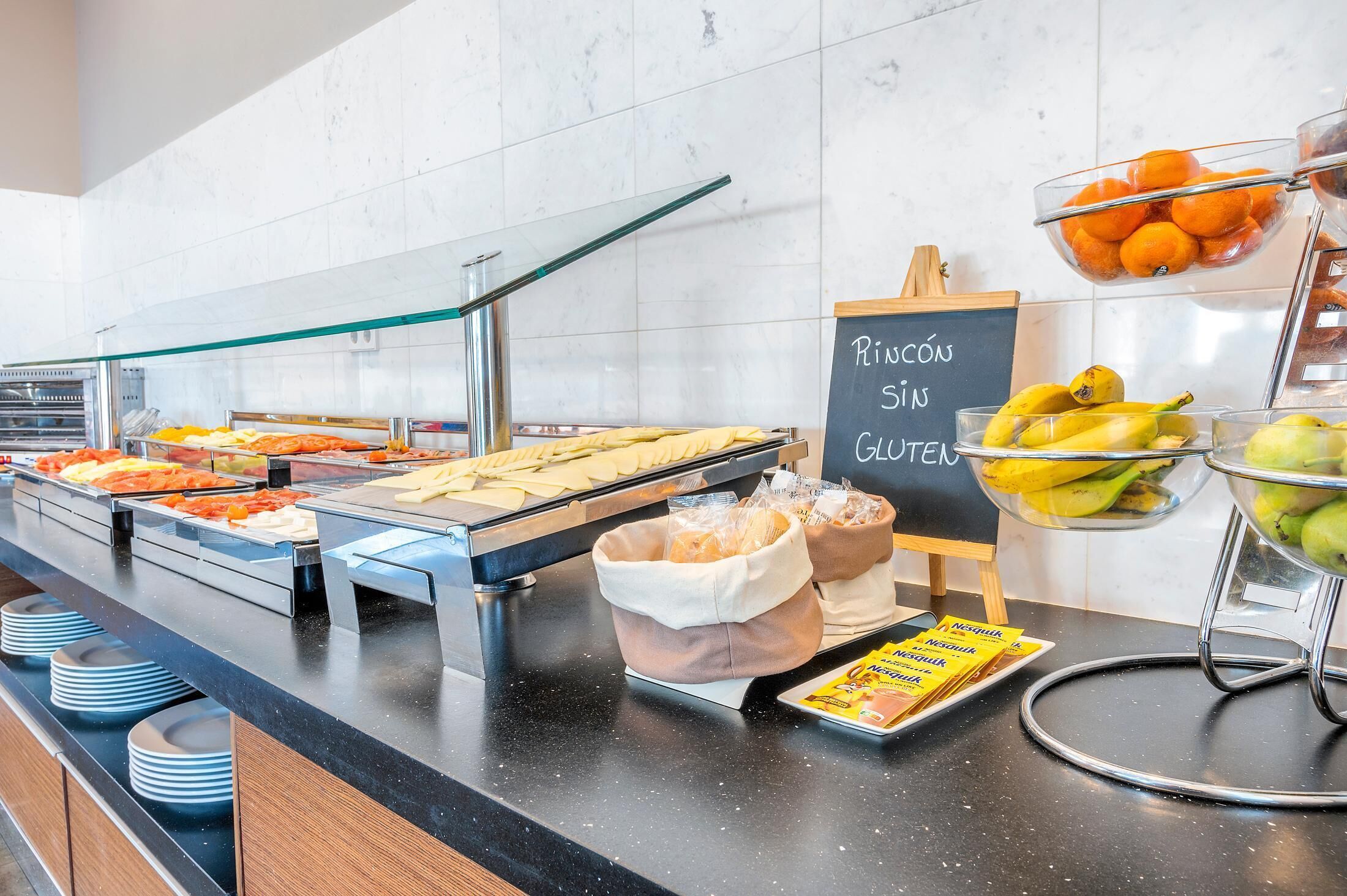 Un buffet con diverse pietanze, tra cui frutta e dolci, e un cartello che indica le opzioni senza glutine.