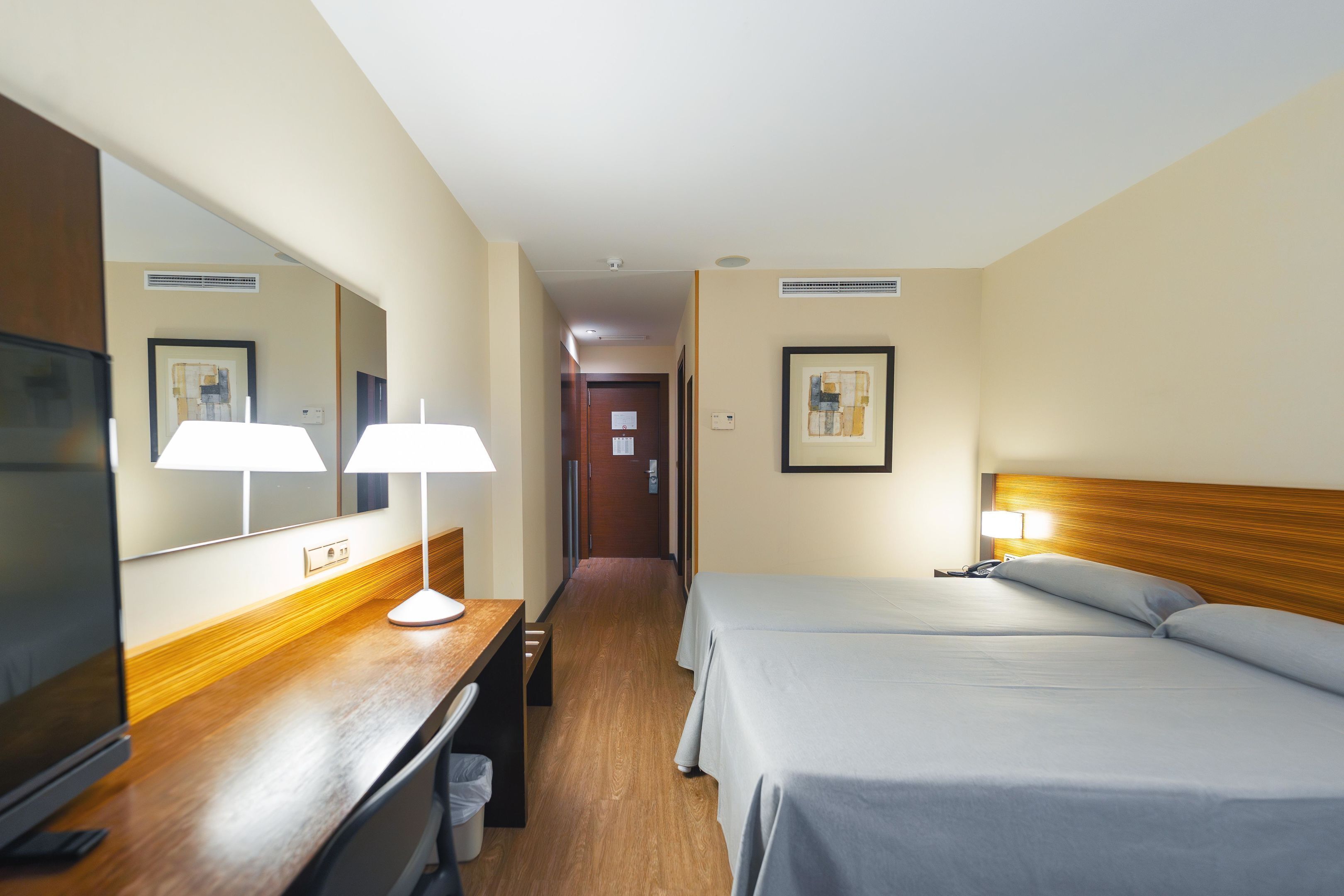 Una habitación de hotel con escritorio de madera, televisor, dos camas y un espejo.