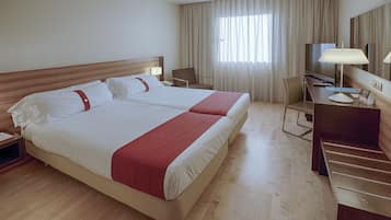 A hotel room with a large bed, a desk, a chair, a TV, and a window with curtains.
