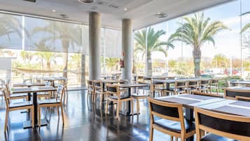 Un amplio comedor interior con ventanas grandes, mesas y sillas de madera.
