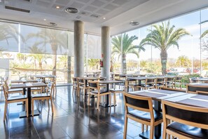 A spacious indoor dining area with large windows, wooden tables, and chairs.