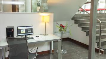 Um espaço de escritório moderno com escrivaninha, computador, cadeira, luminária e um vaso com flores.