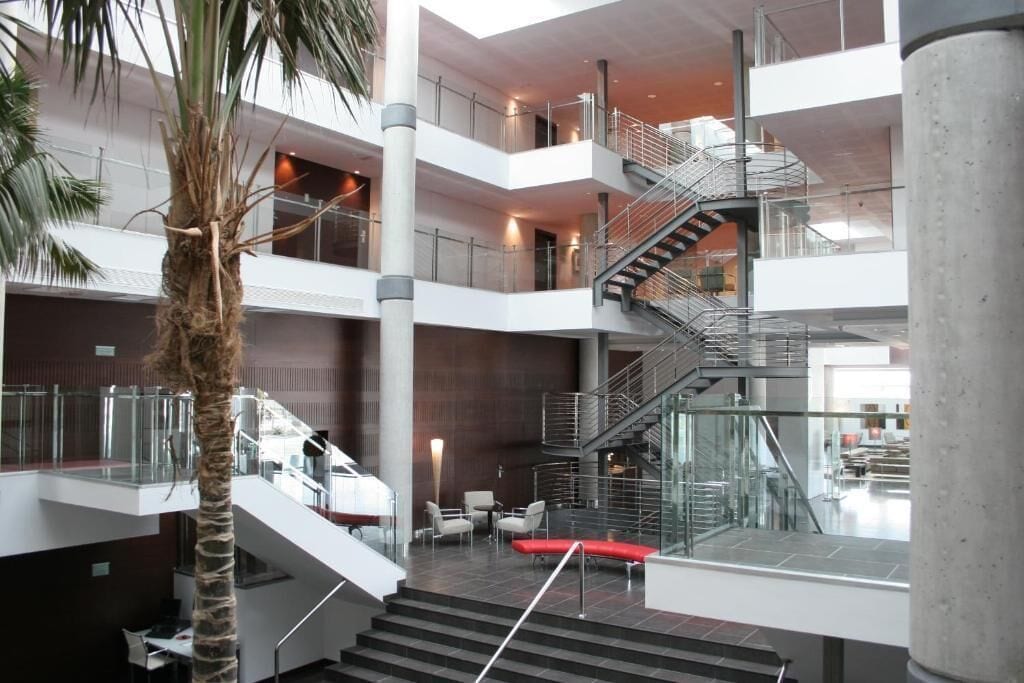 Ein mehrgeschossiges Atrium mit einer zentralen Treppe, Glasgeländern und Sitzbereichen.