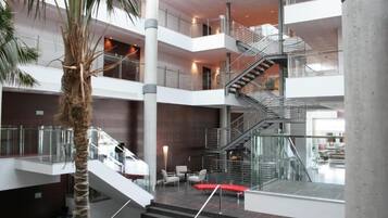 Ein mehrgeschossiges Atrium mit einer zentralen Treppe, Glasgeländern und Sitzbereichen.