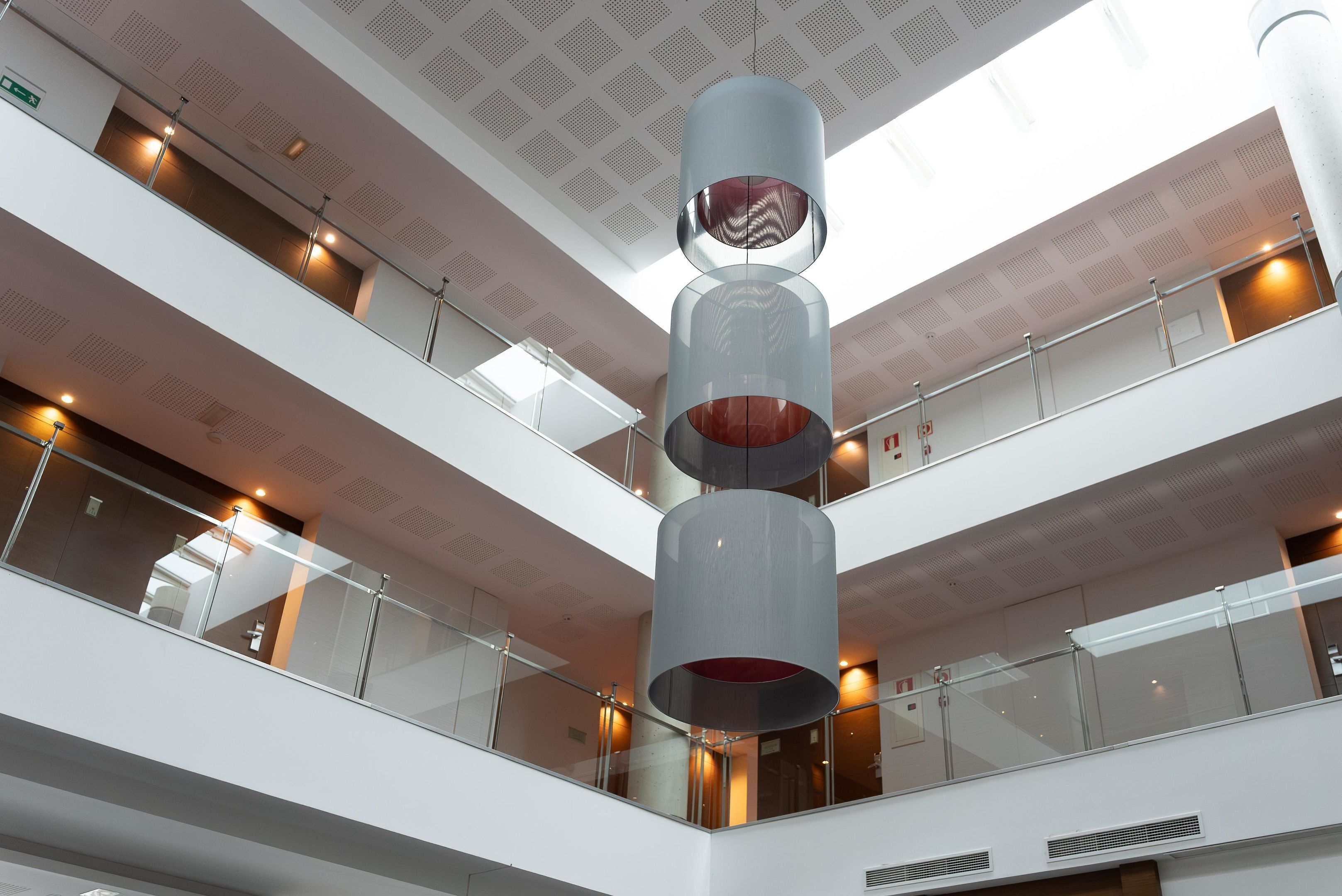 A multi-level atrium with a central cylindrical structure, glass railings, and a ceiling with a grid pattern.