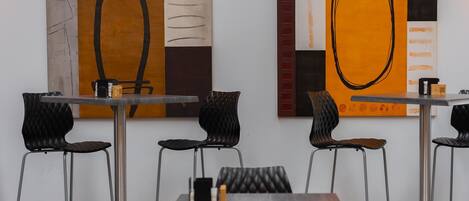 Ein modernes Restaurant-Interieur mit minimalistischer Einrichtung, schwarze, gepolsterte Stühle und Tische sowie abstrakte Kunstwerke an den Wänden.
