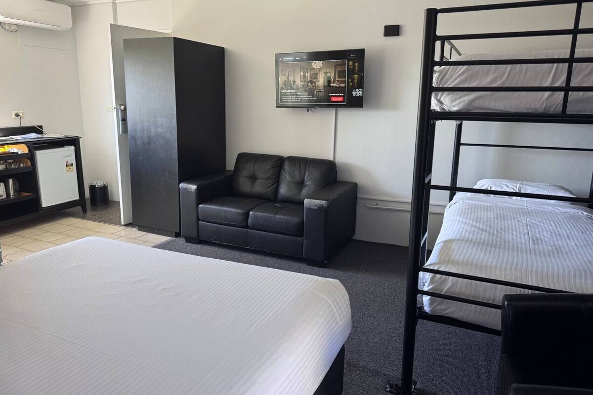 A hotel room with a bunk bed, a sofa, a desk with a computer, and a TV mounted on the wall.