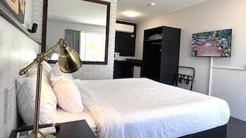 Una habitació d'hotel amb un llit gran, una taula de nit amb una làmpada, una televisió a la paret i un armari.