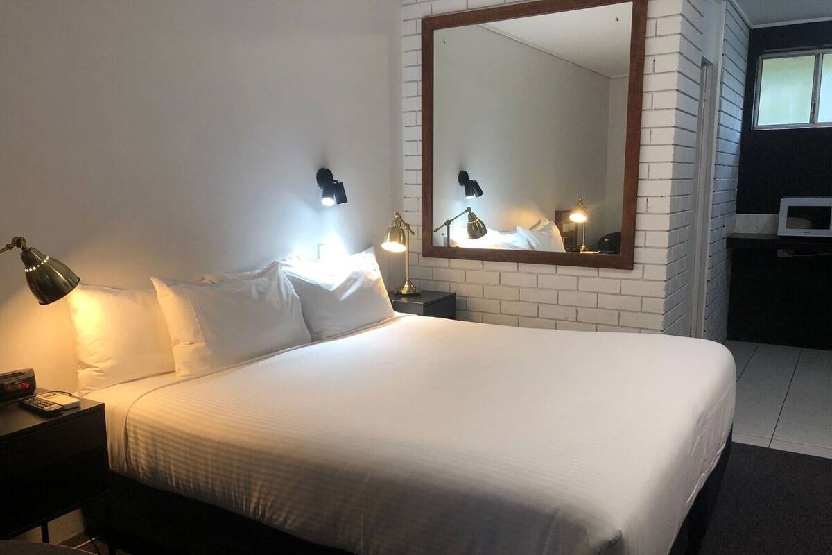 A hotel room with a large bed, two bedside tables, a nightstand, a desk, a chair, a mirror, and a TV.
