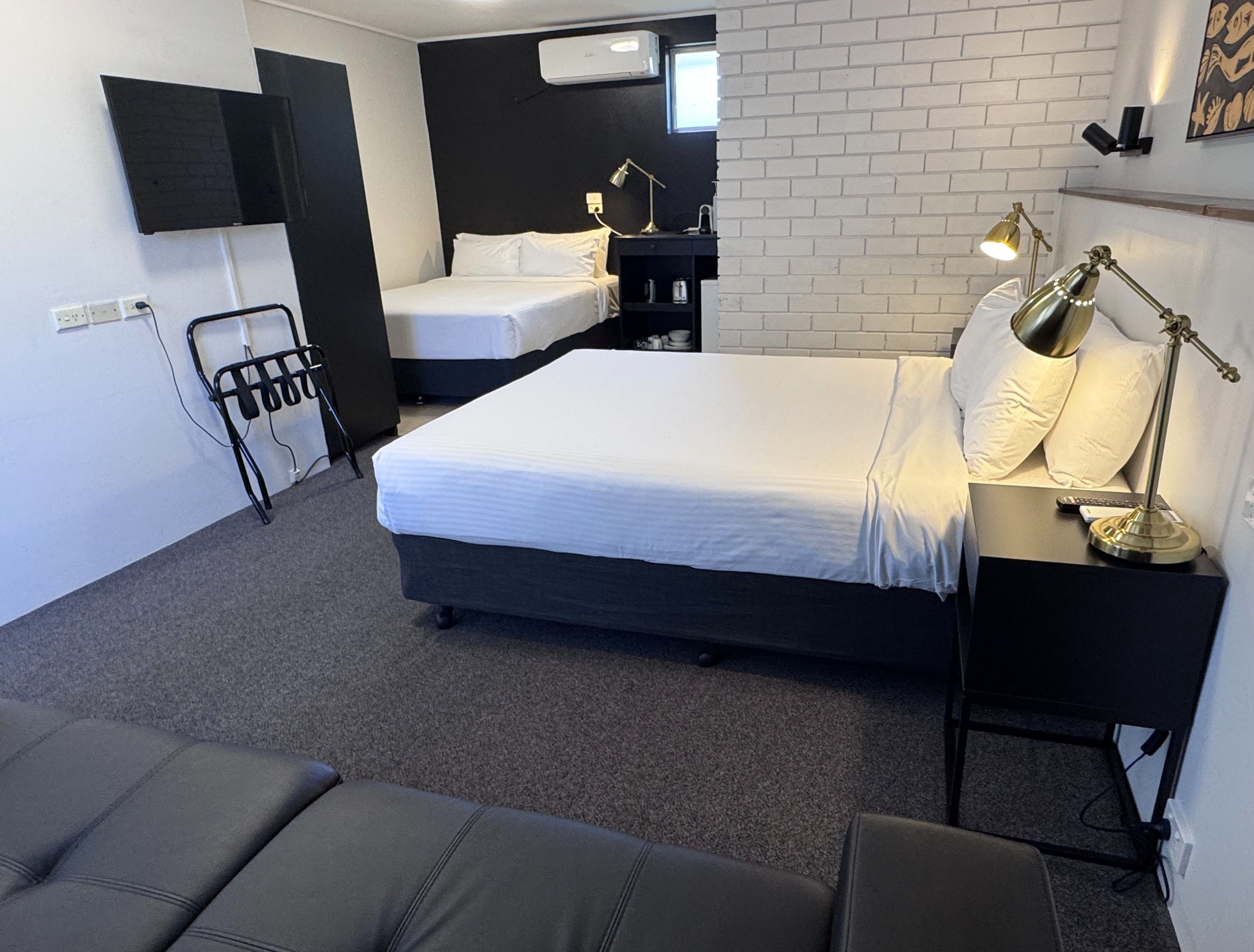 Une chambre d’hôtel comprenant un lit, des tables de chevet, un bureau, une chaise, une télévision et un climatiseur fixé au mur.
