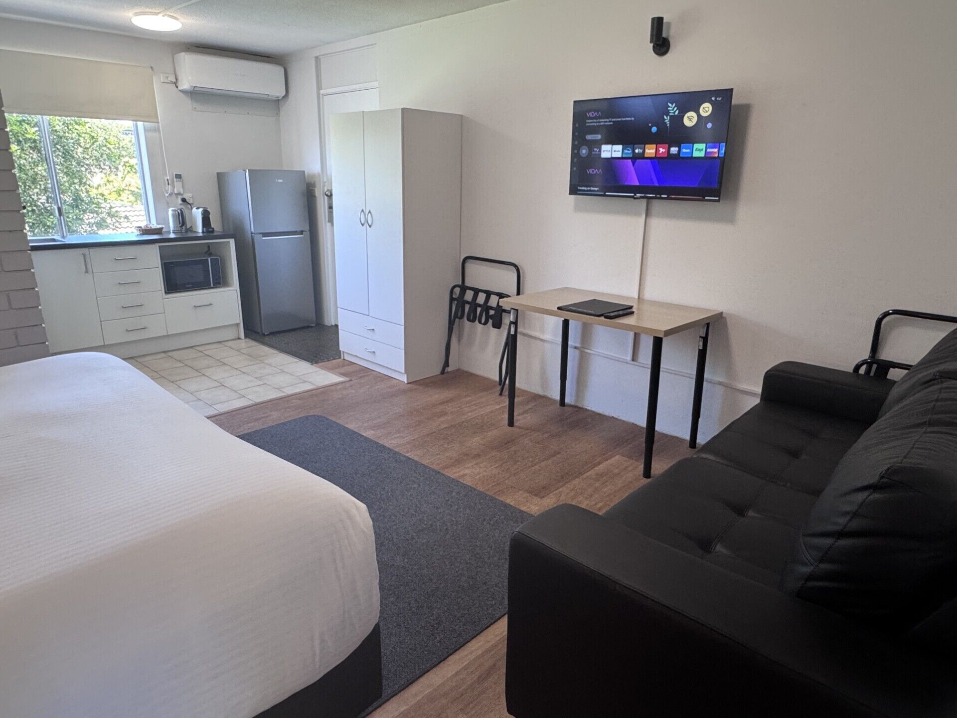 A compact room with a bed, a desk, a TV, a kitchenette, and a wardrobe.