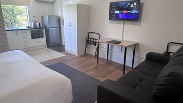 A compact room with a bed, a desk, a TV, a kitchenette, and a wardrobe.