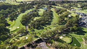 An aerial view of a golf course with bunkers, water hazards, and a parking area. - Matador Motor Inn (Coffs Harbour)