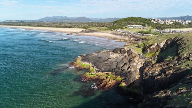 A coastal landscape with clear waters, rocky cliffs, and a distant beach with buildings. - Matador Motor Inn (Coffs Harbour)