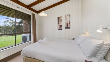 A bedroom with a large bed, a window with blinds, a wall-mounted air conditioner, and two framed pictures.