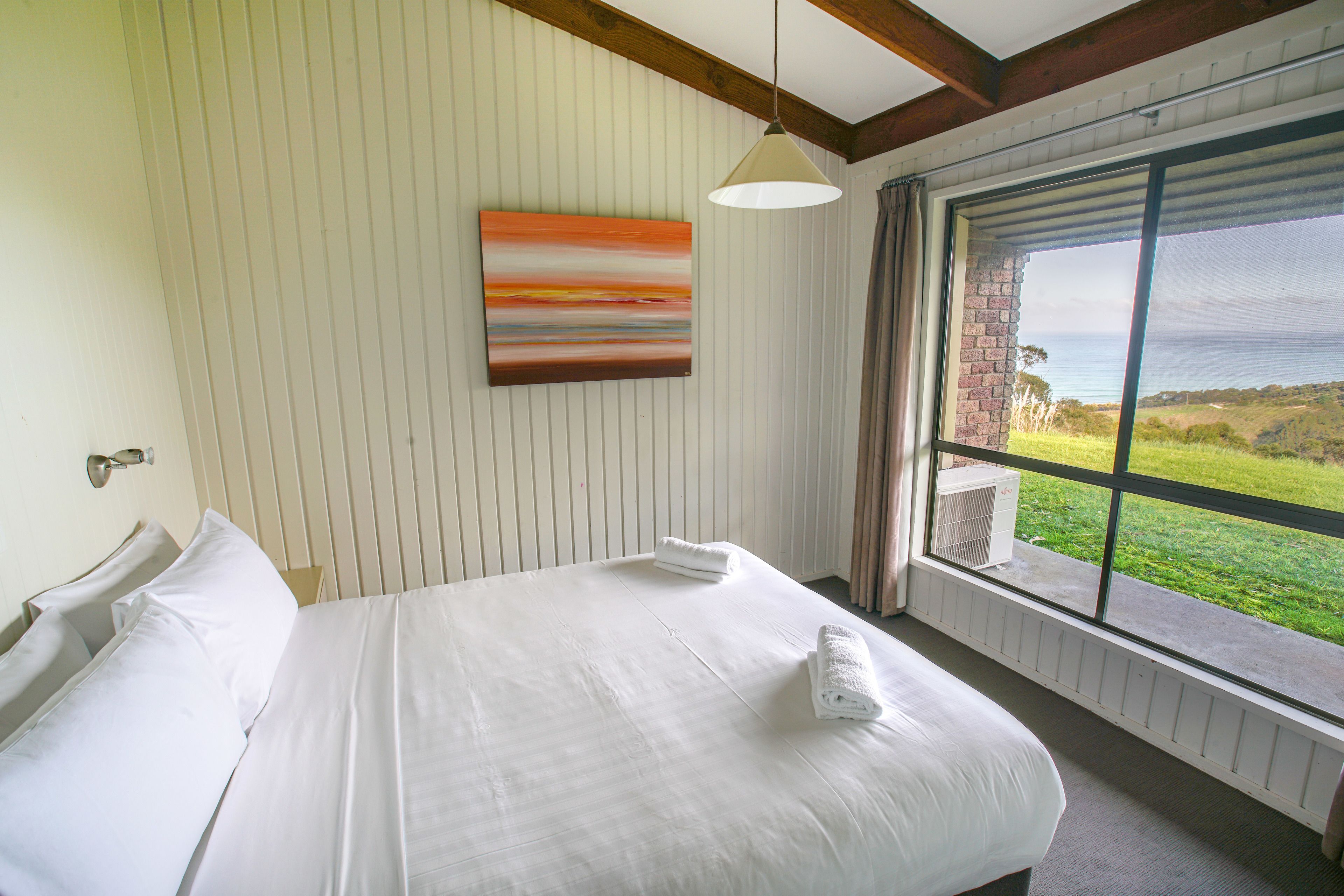 Een hotelkamer met een groot bed, een schilderij aan de muur en uitzicht op zee door een raam.