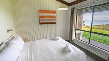 Een hotelkamer met een groot bed, een schilderij aan de muur en uitzicht op zee door een raam.