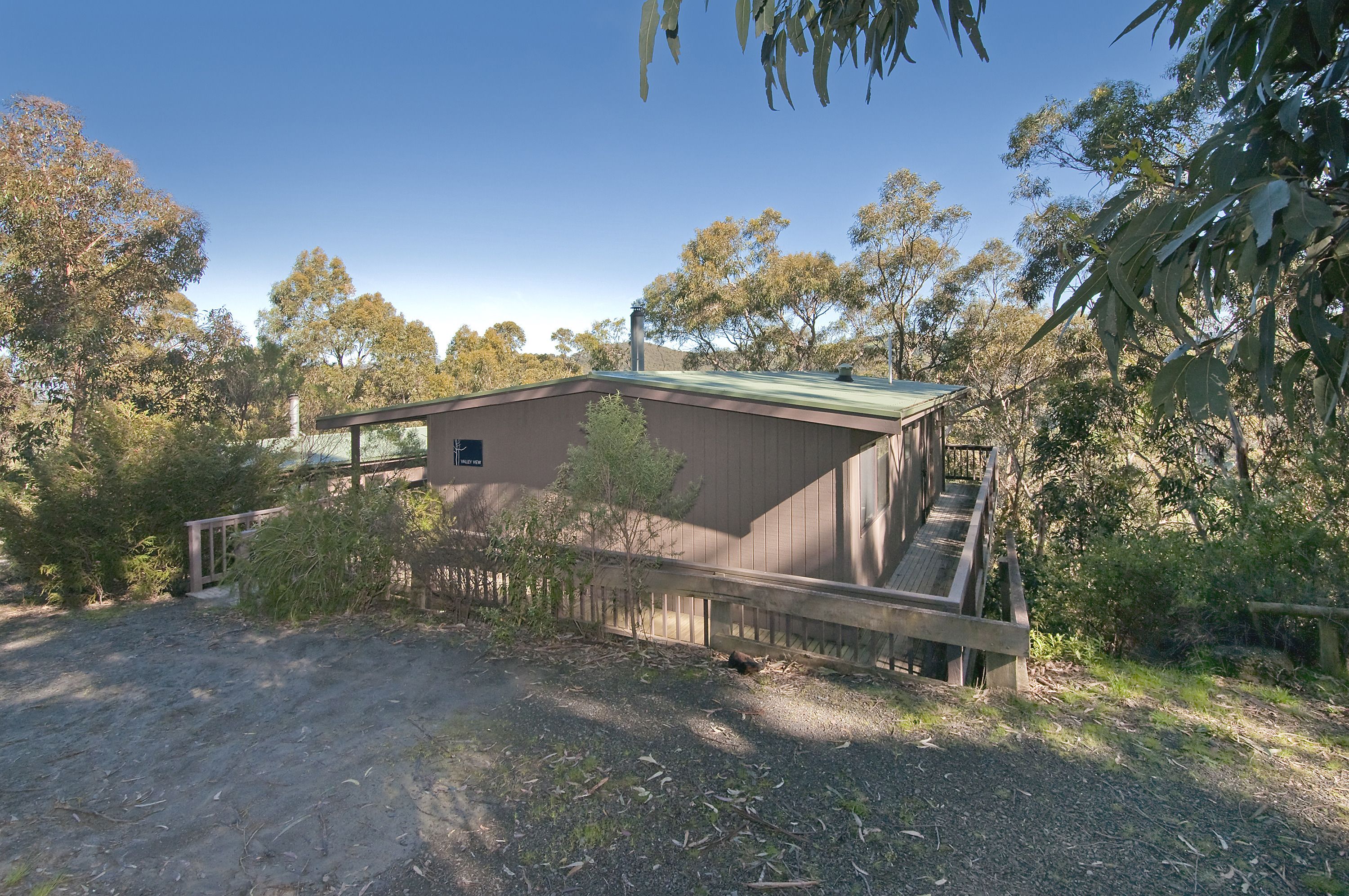 A single-story building with a green roof, surrounded by trees and a gravel driveway.