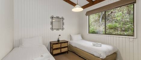 A bedroom with two beds, a nightstand, a mirror, and a window with a view of greenery.