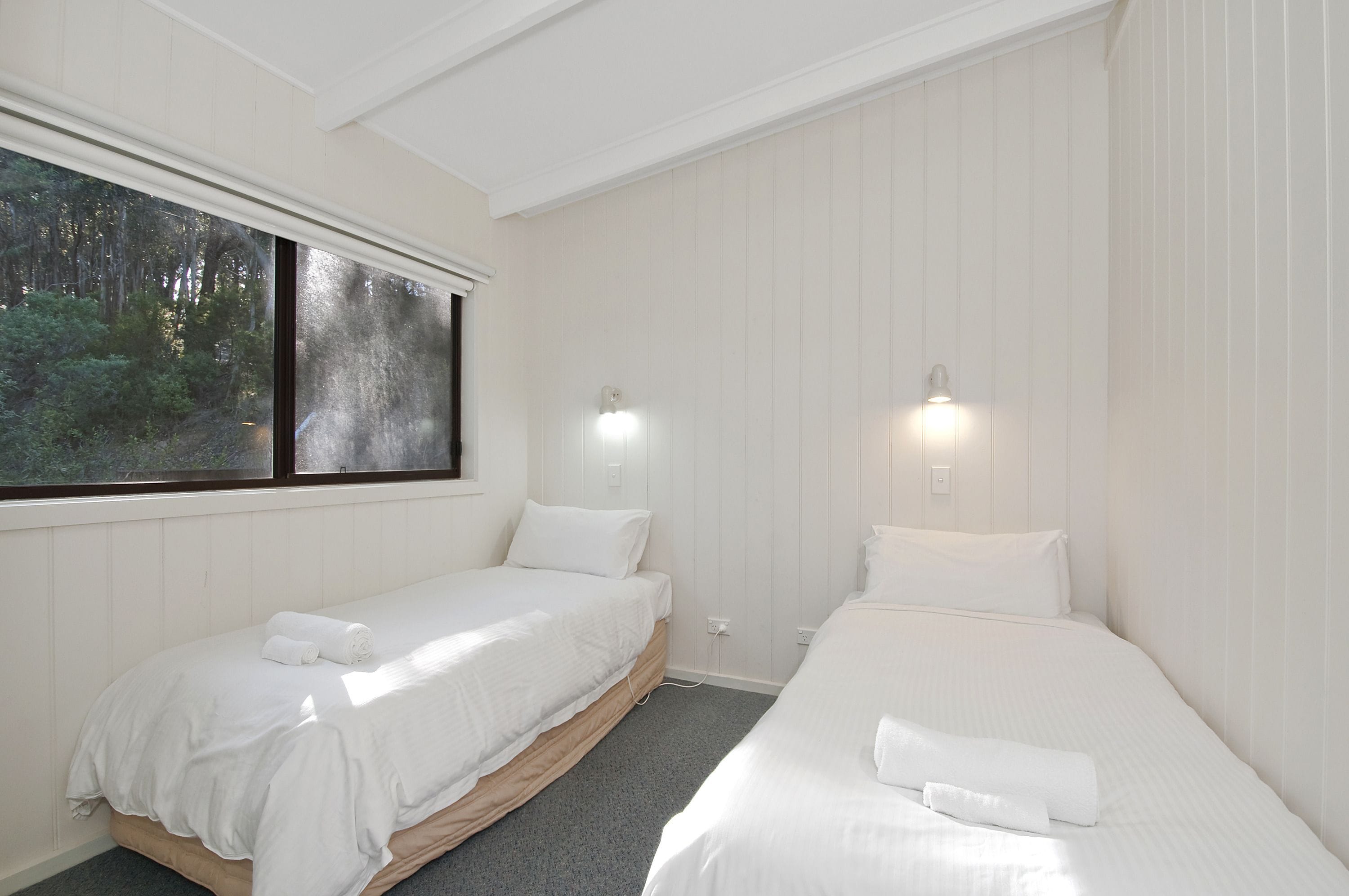 Ein Zimmer mit zwei Einzelbetten, einem großen Fenster mit Blick auf Bäume und Wandleuchten.