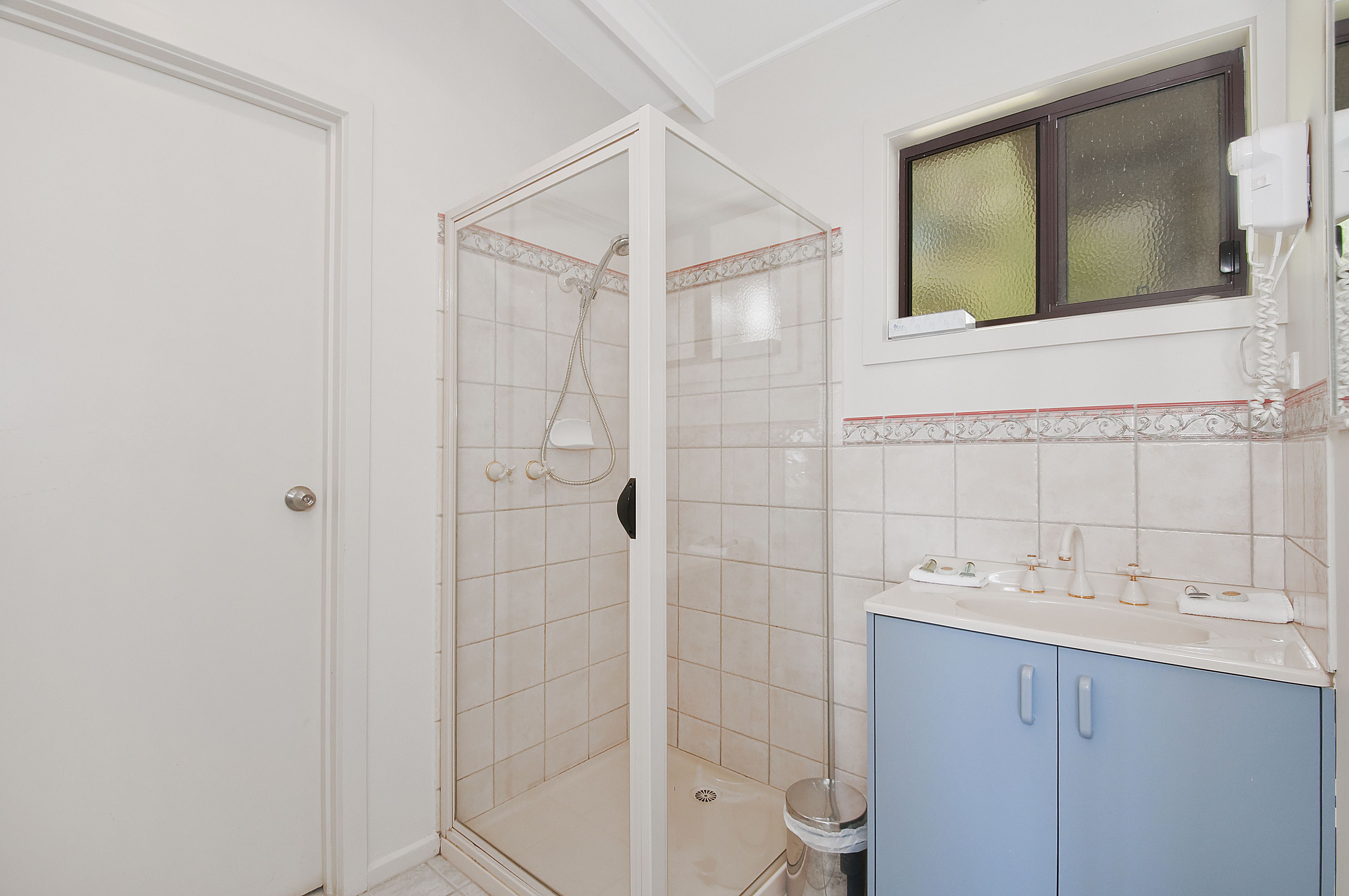 A bathroom with a glass-enclosed shower, a sink with a mirror, and a window above the sink.