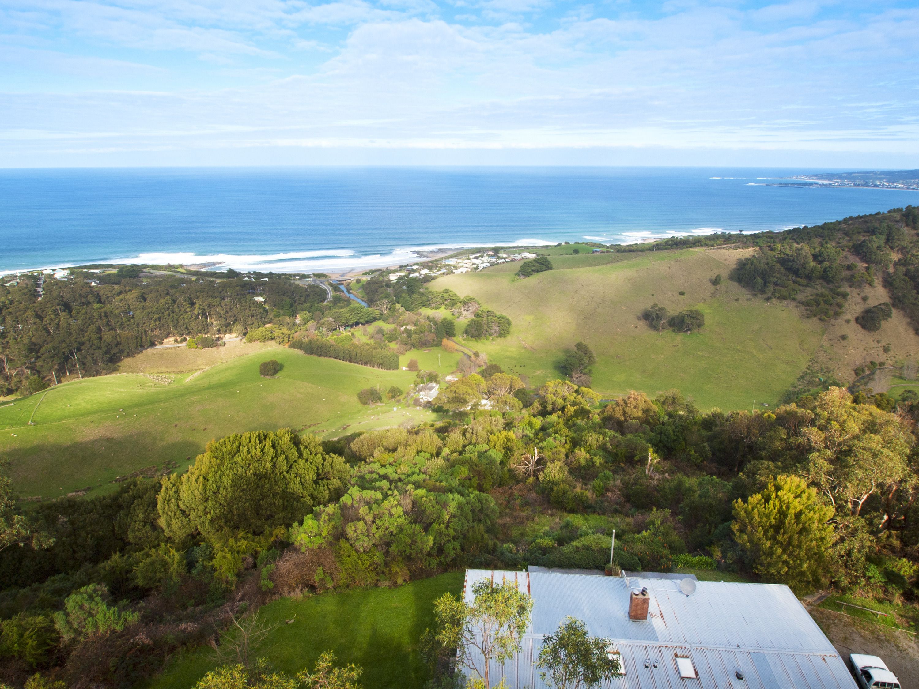 A coastal landscape with a view of the ocean, green fields, and a building with a metal roof.