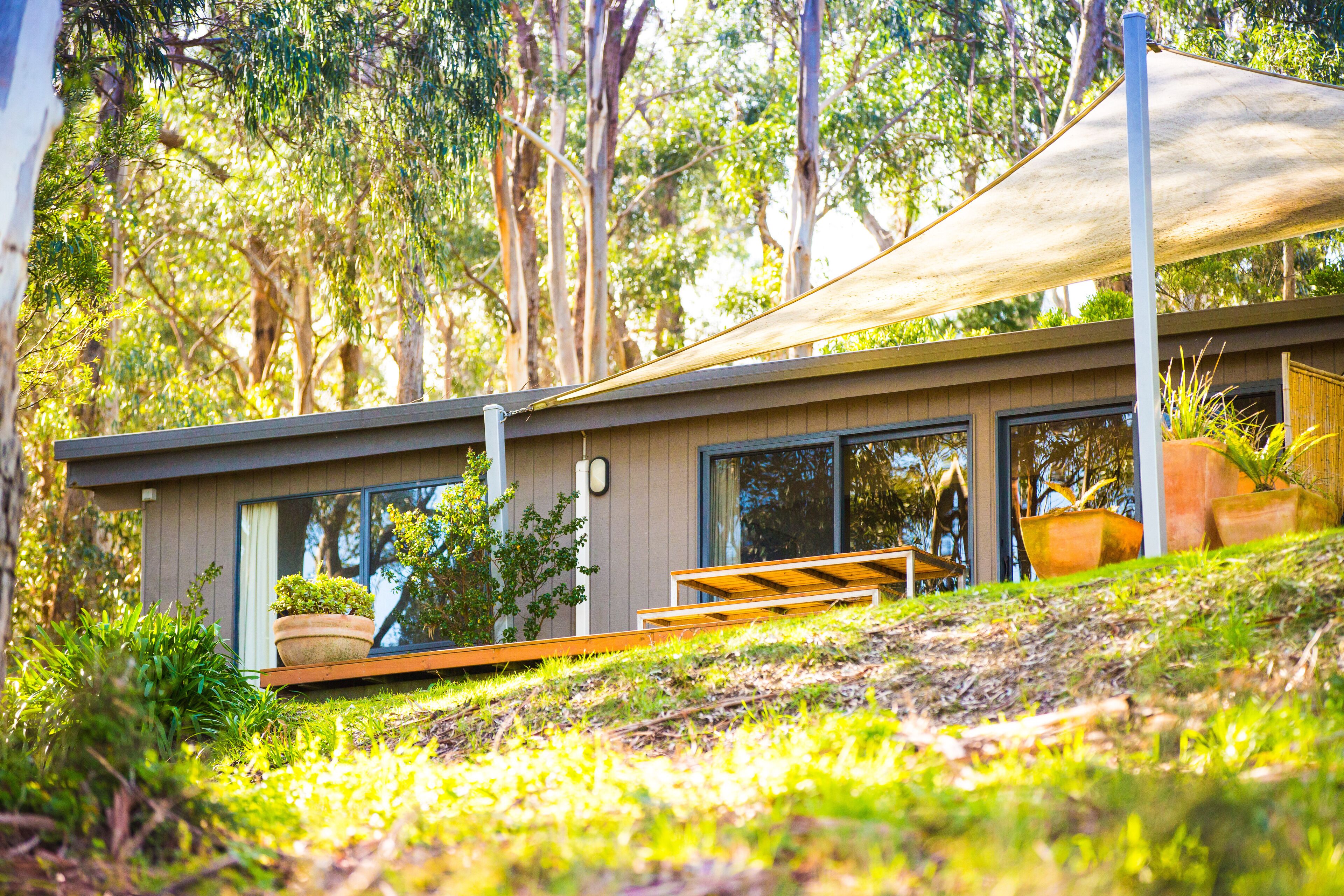 A modern house with large windows, a wooden deck, and a shaded area.