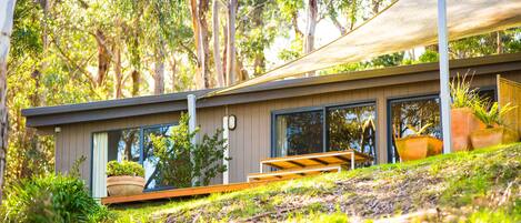 A modern house with large windows, a wooden deck, and a shaded area.
