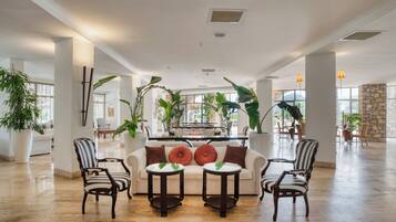 A spacious lobby with a central seating area, large windows, and potted plants.