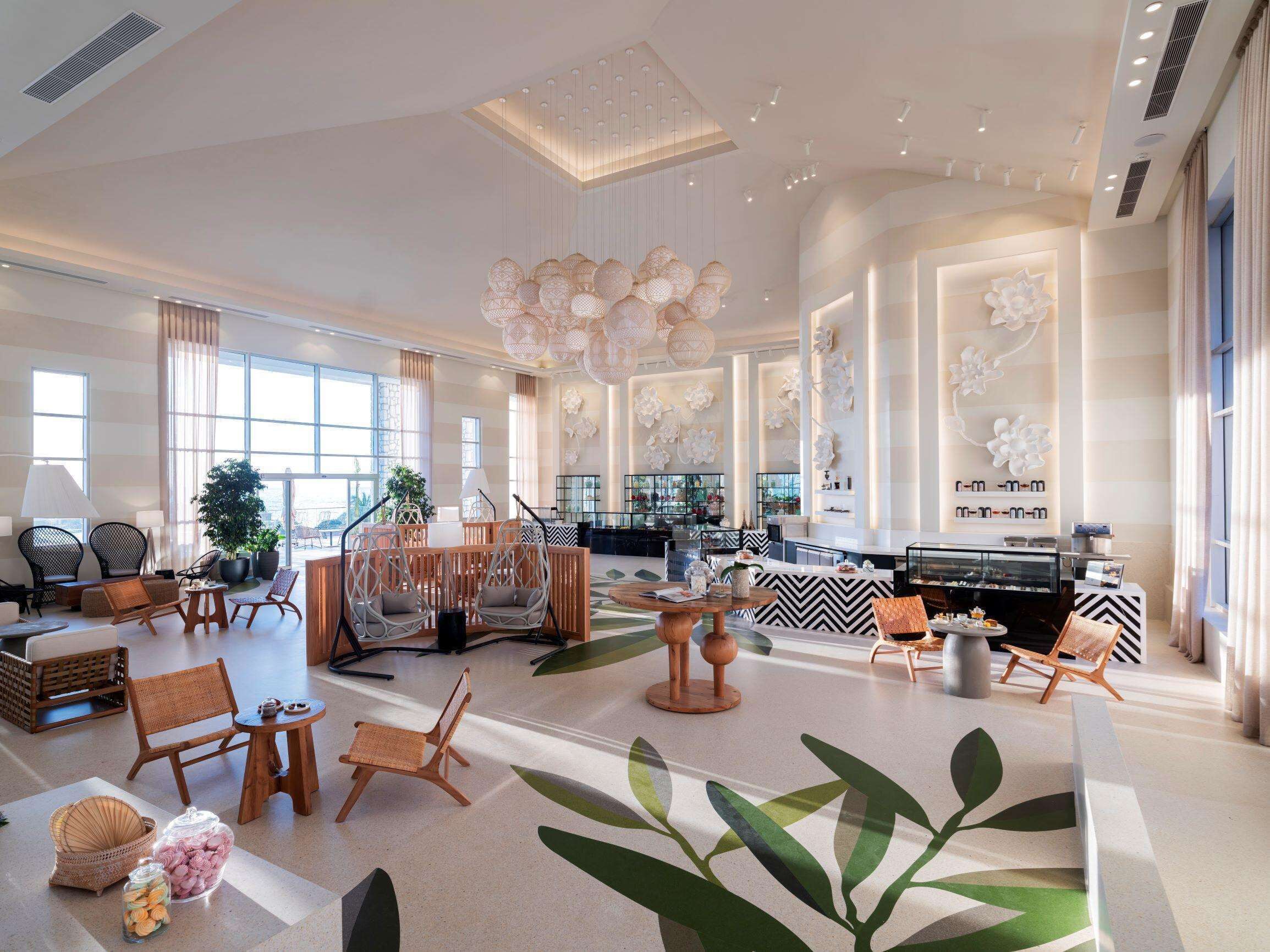 A spacious hotel lobby with a central seating area, large windows, and a modern chandelier.