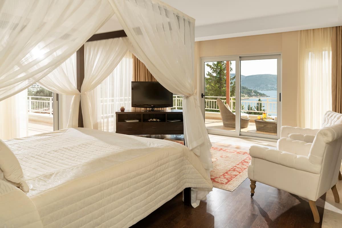 A bedroom with a bed, a TV, a chair, and a balcony with a view.