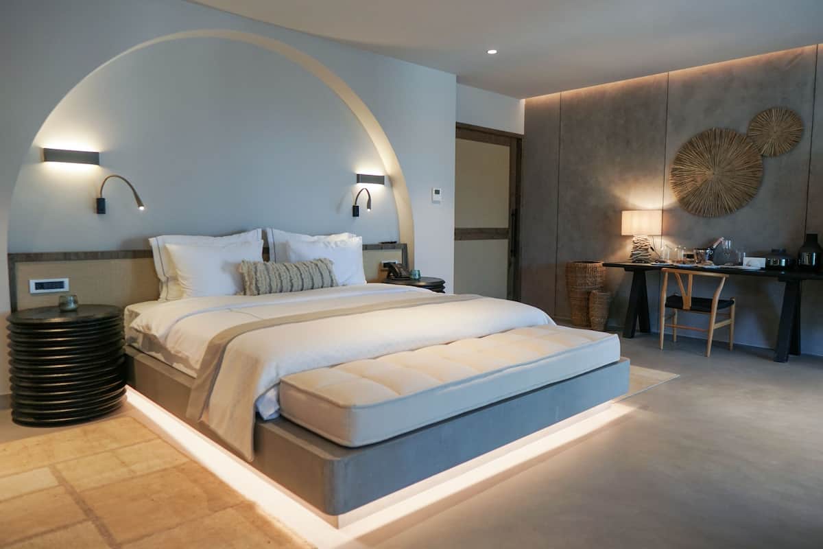 A modern bedroom with a large bed, bedside lamps, a desk, and a chair.