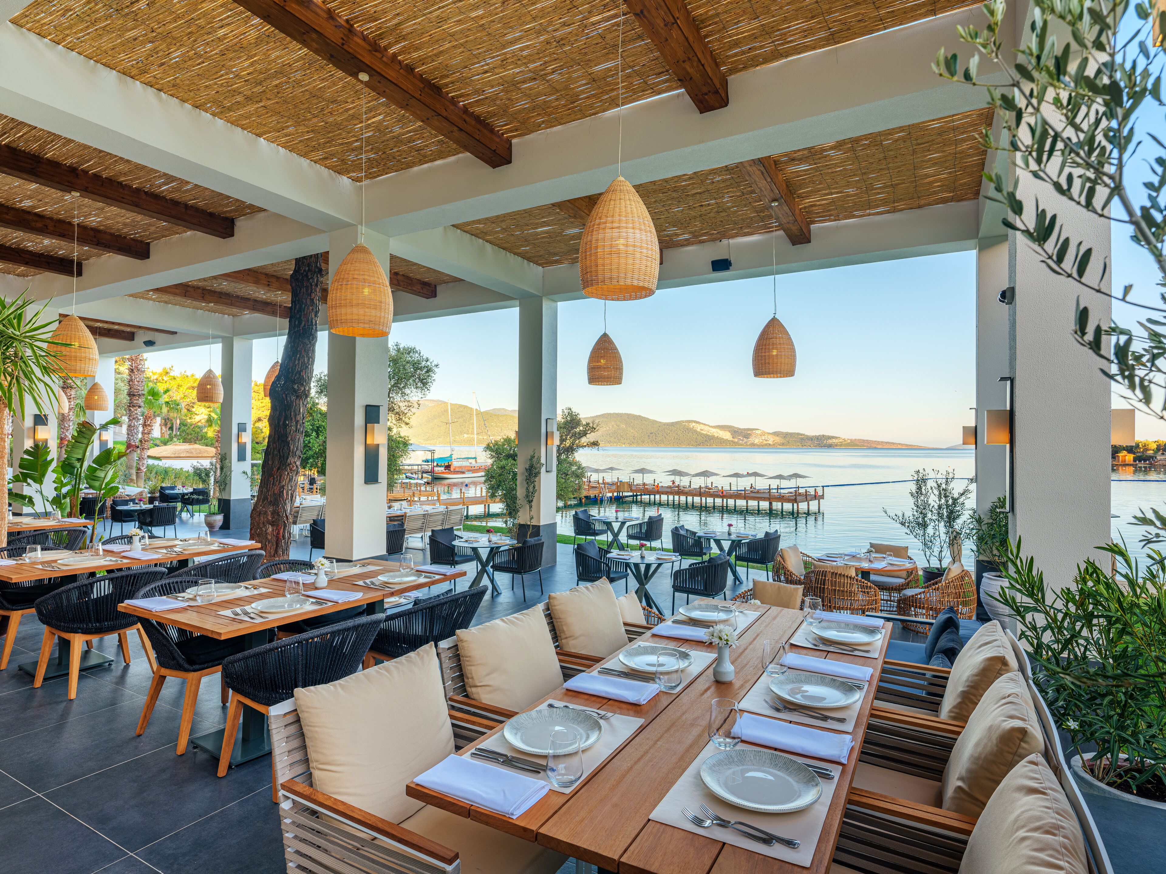 An outdoor dining area with tables set for two, overlooking a body of water.