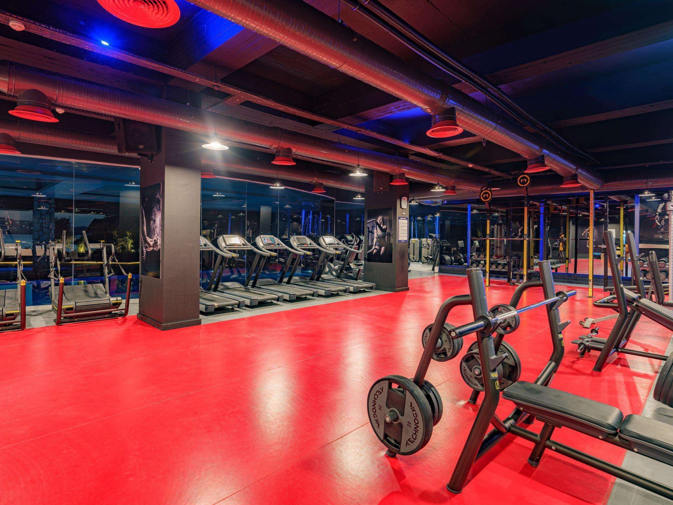 A gym with treadmills, weight machines, and a red floor.