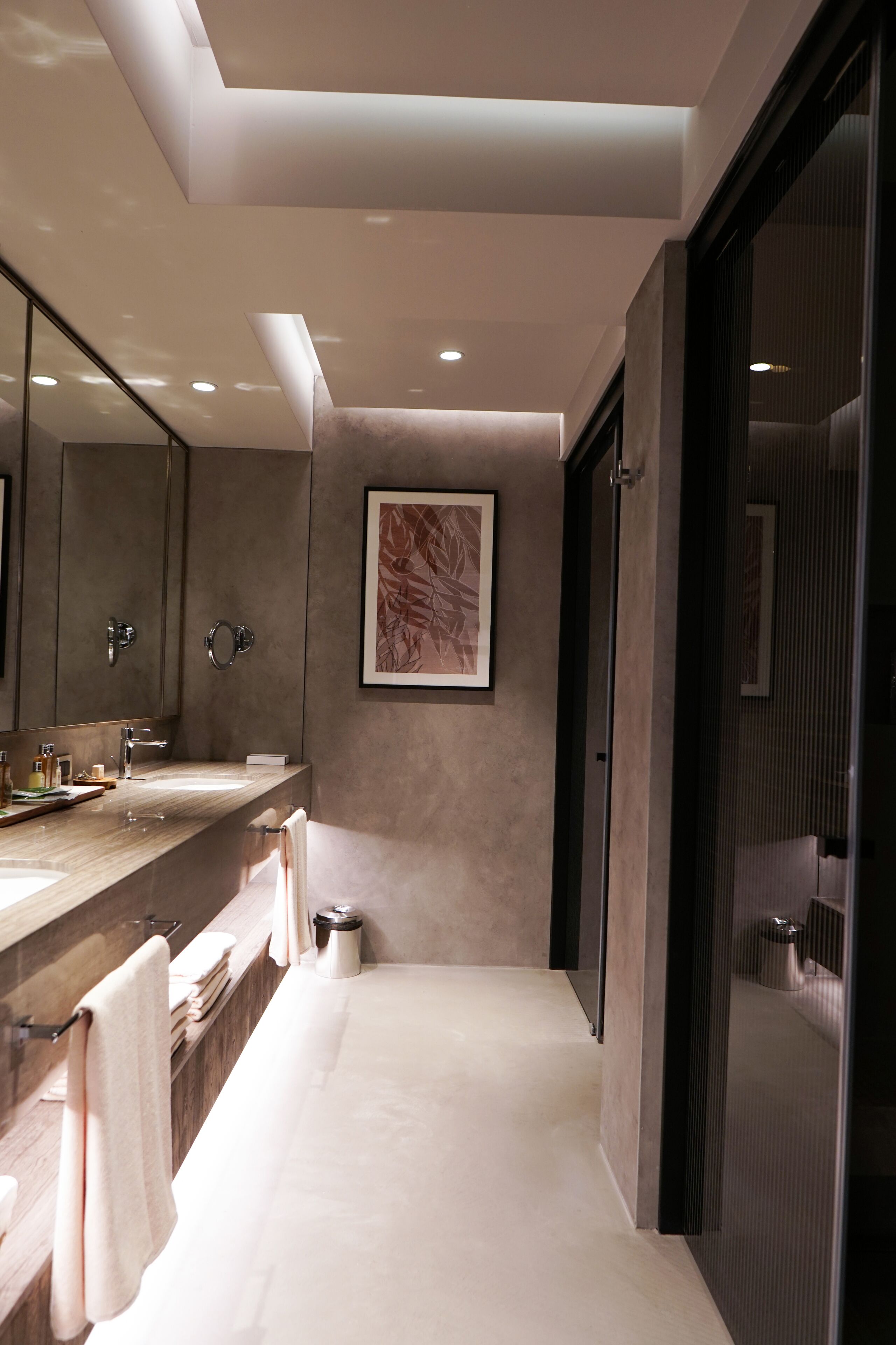 A modern bathroom with a large mirror, two sinks, a towel rack, and a framed artwork on the wall.