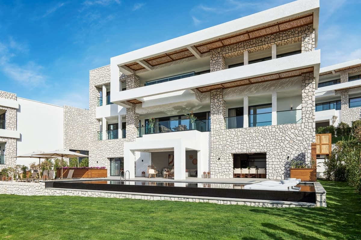 A modern multi-story building with a stone facade, outdoor seating area, and a swimming pool.
