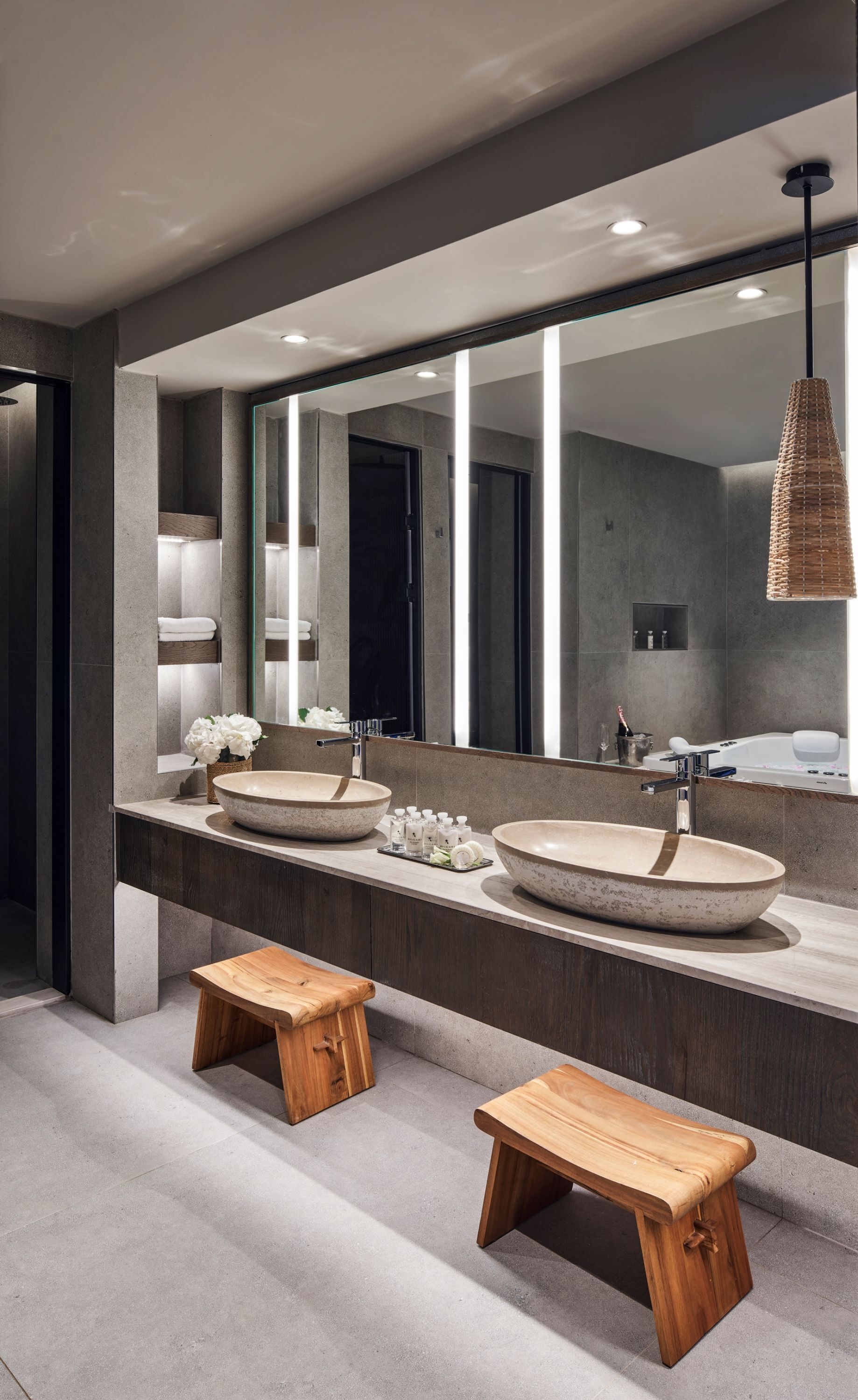Une salle de bain moderne avec deux grands lavabos sur pied, un grand miroir et des tabourets en bois.
