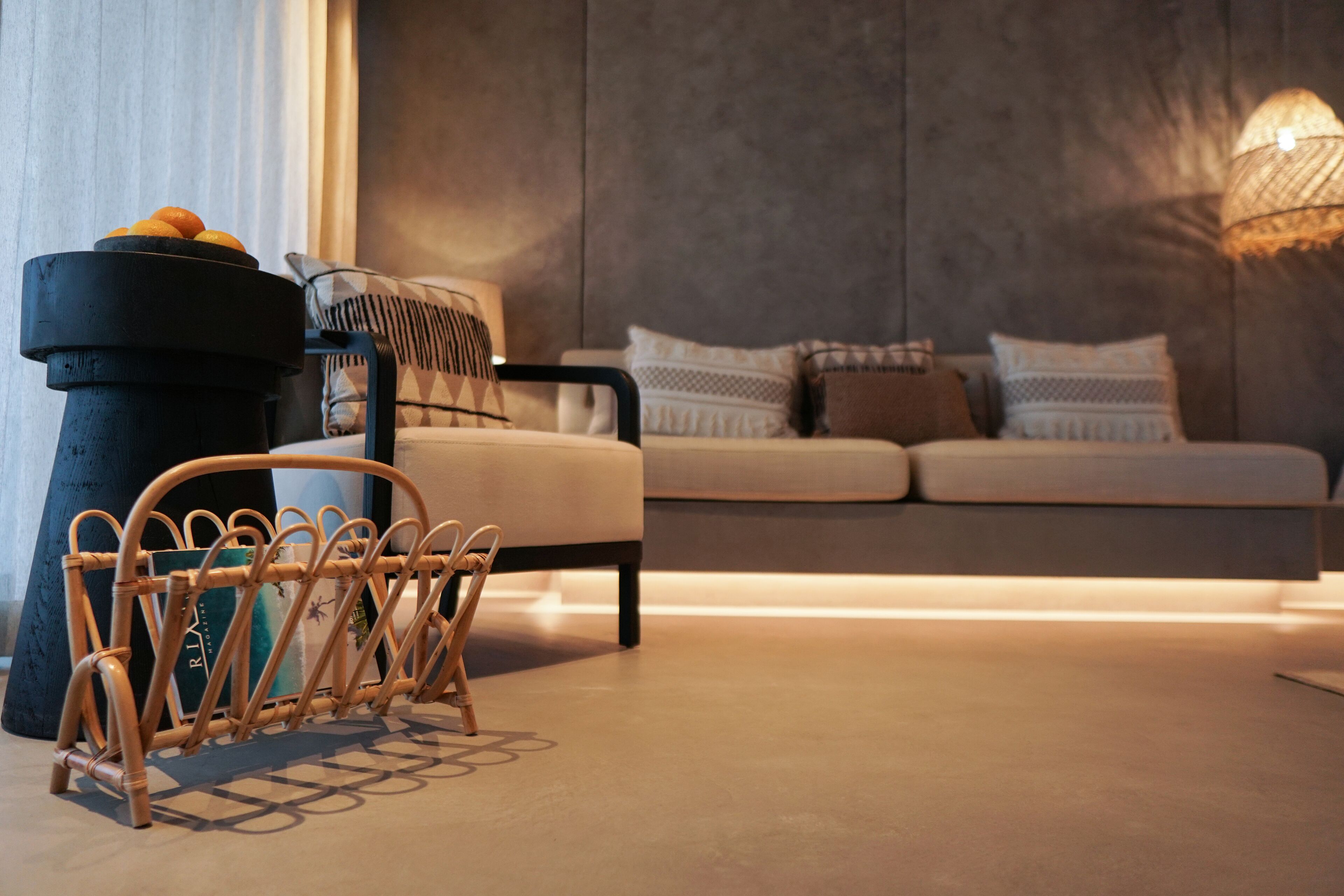A modern living room with a sofa, a wicker chair, and a black planter with oranges.