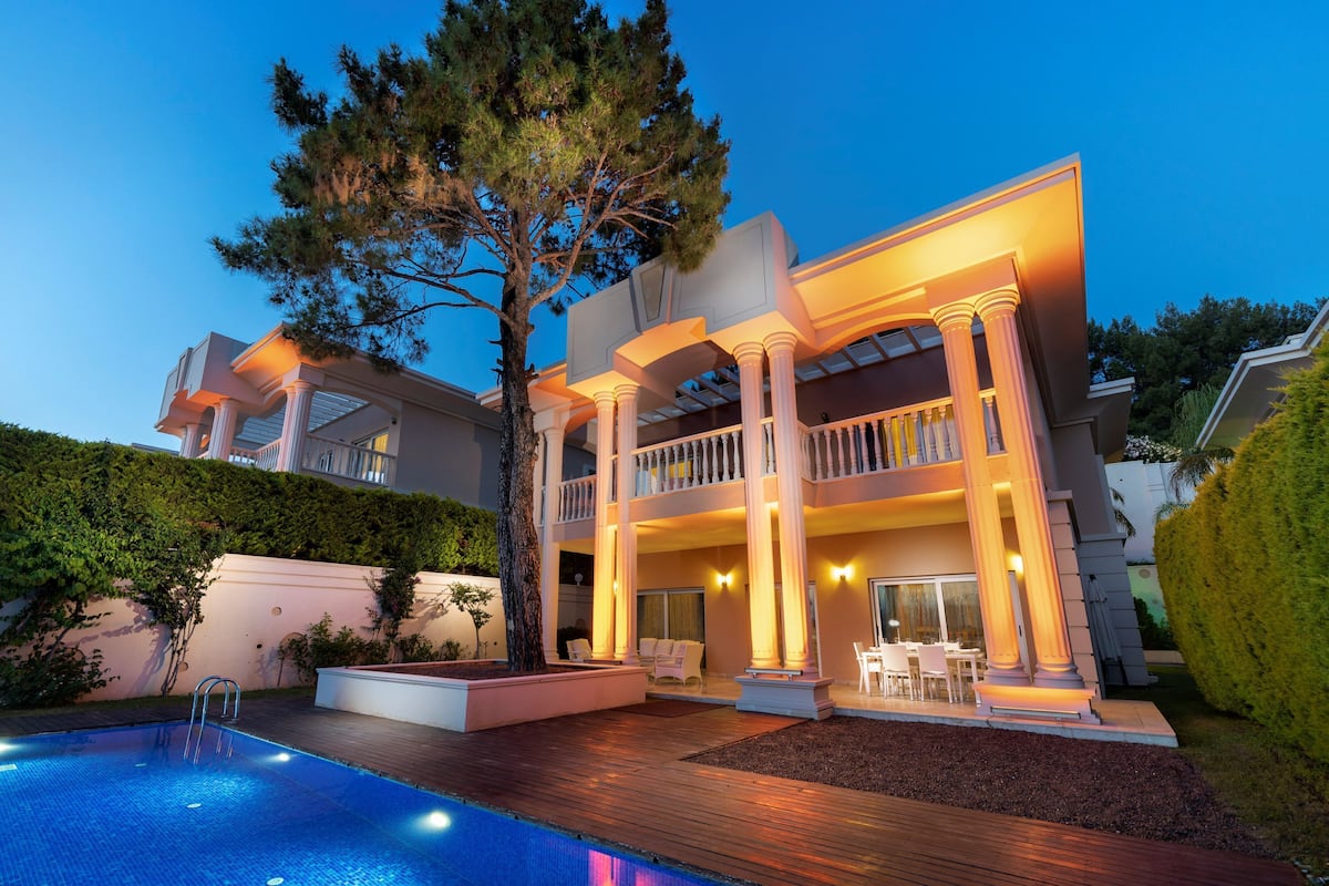 A large, two-story house with a swimming pool, outdoor seating, and a well-lit balcony.