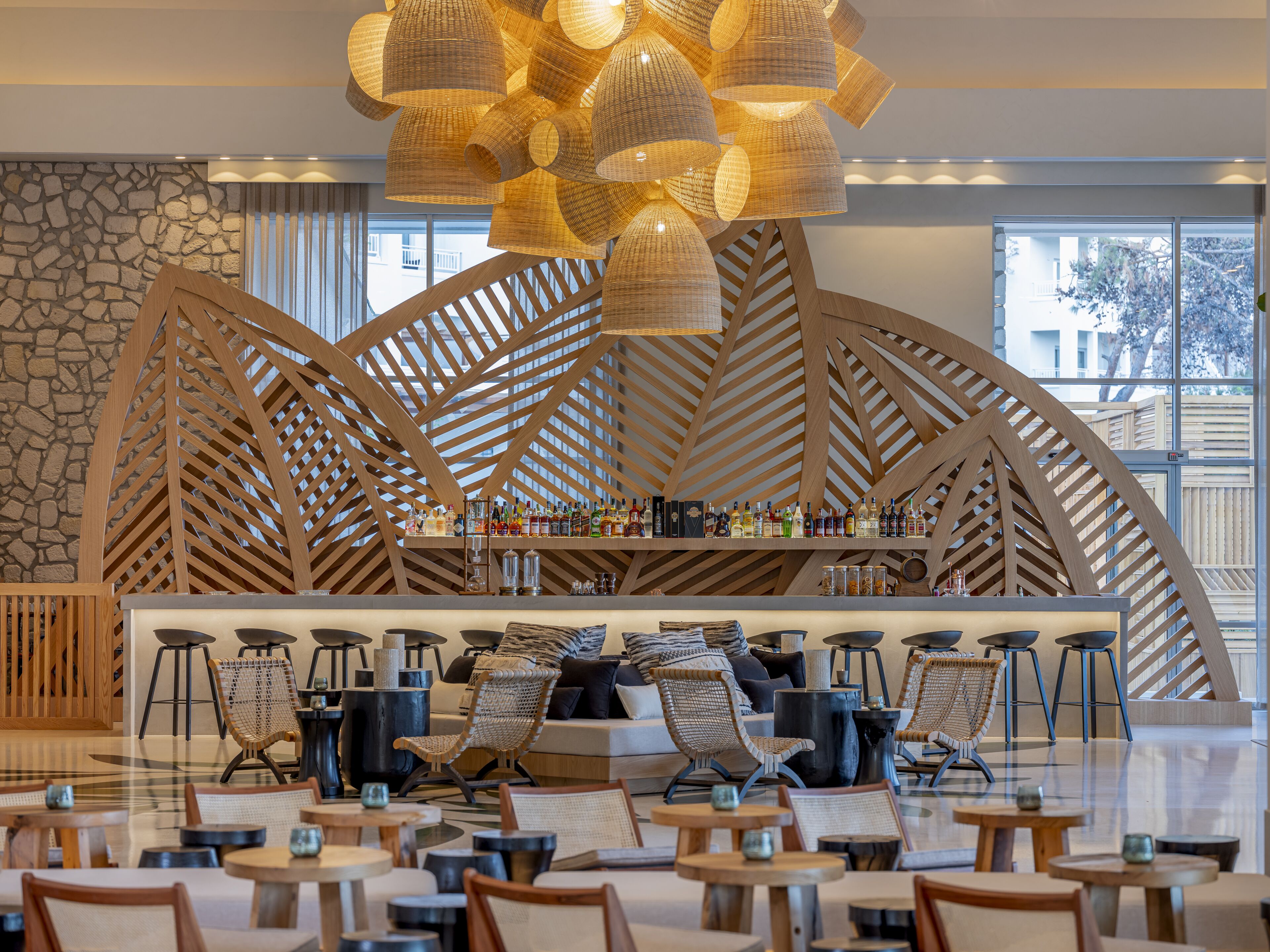 Un bar moderno con techo de celosía de madera, gran variedad de botellas y asientos con sillas y mesas de mimbre.