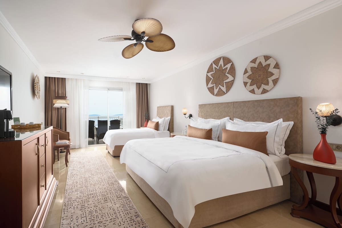 A hotel room with two beds, a desk, a dresser, a ceiling fan, and decorative wall art.